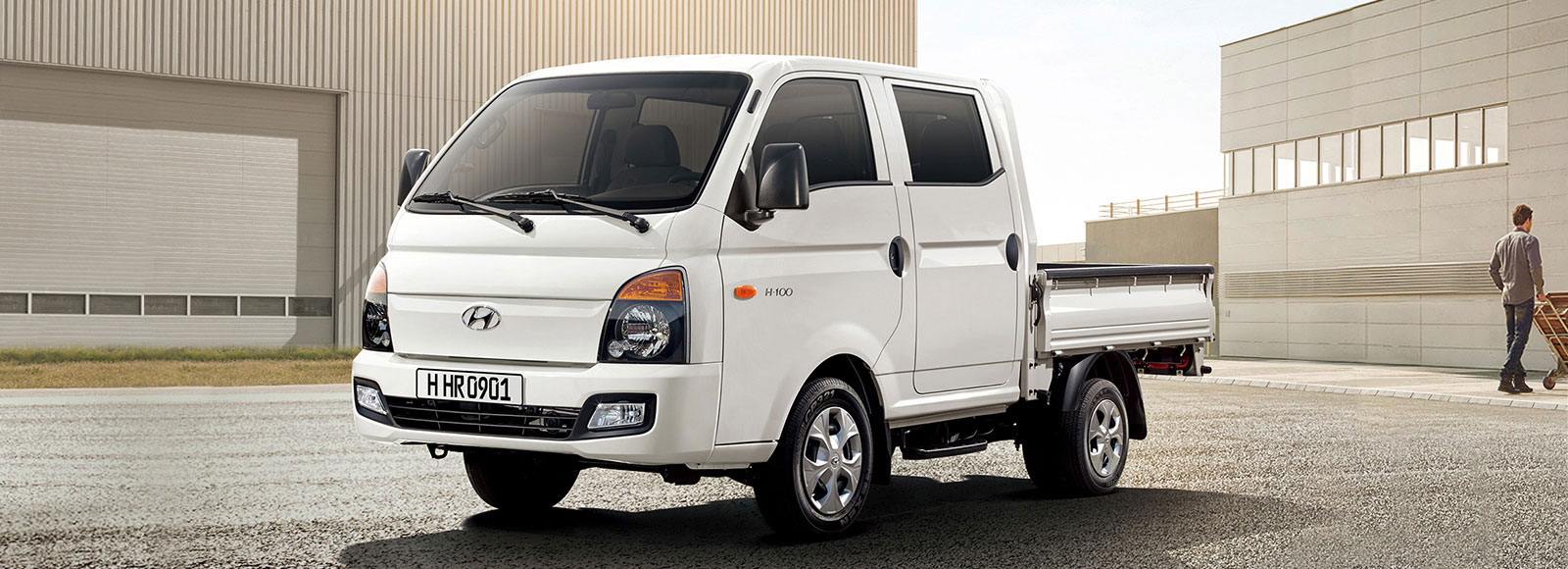 A front view of white H-100 with a person and buildings behind